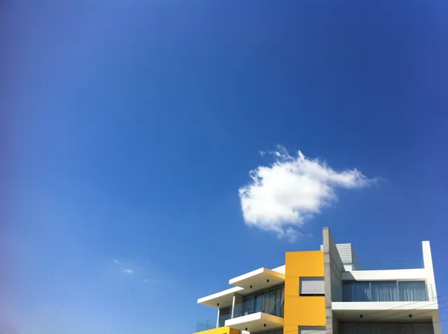 Λευκό και κίτρινο κτίριο κάτω από καθαρό μπλε ουρανό με ένα μικρό σύννεφο.