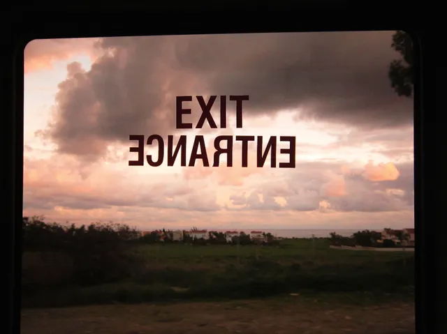 Οι λέξεις EXIT και ENTRANCE σε τζάμι μπροστά σε συννεφιασμένο ηλιοβασίλεμα.