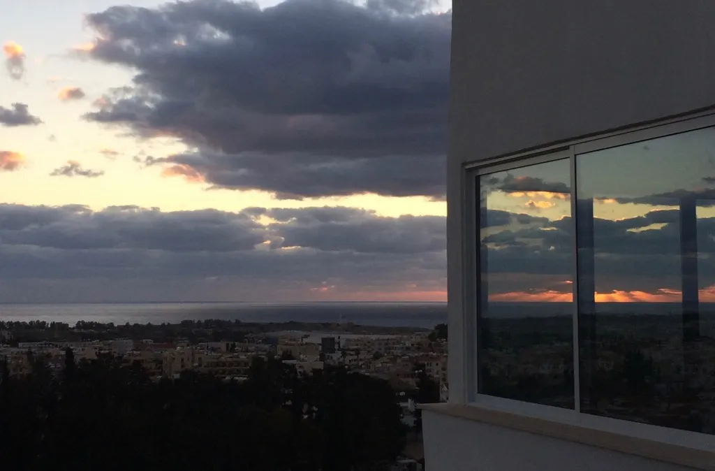 Ηλιοβασίλεμα πάνω από την πόλη και τη θάλασσα, με αντανάκλαση στα παράθυρα