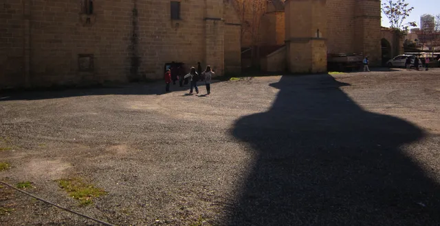 Μικρή ομάδα ανθρώπων μπροστά σε μεγάλο πέτρινο κτίριο, δίπλα σε μακριά σκιά.